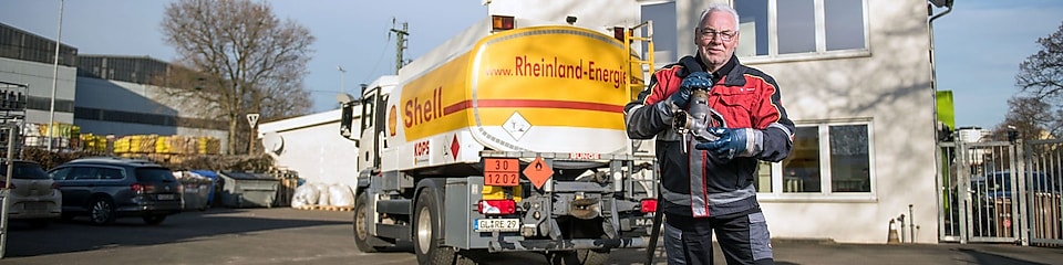Tankwagenfahrer steht vor Shell Tankwagen und traegt Schlauch