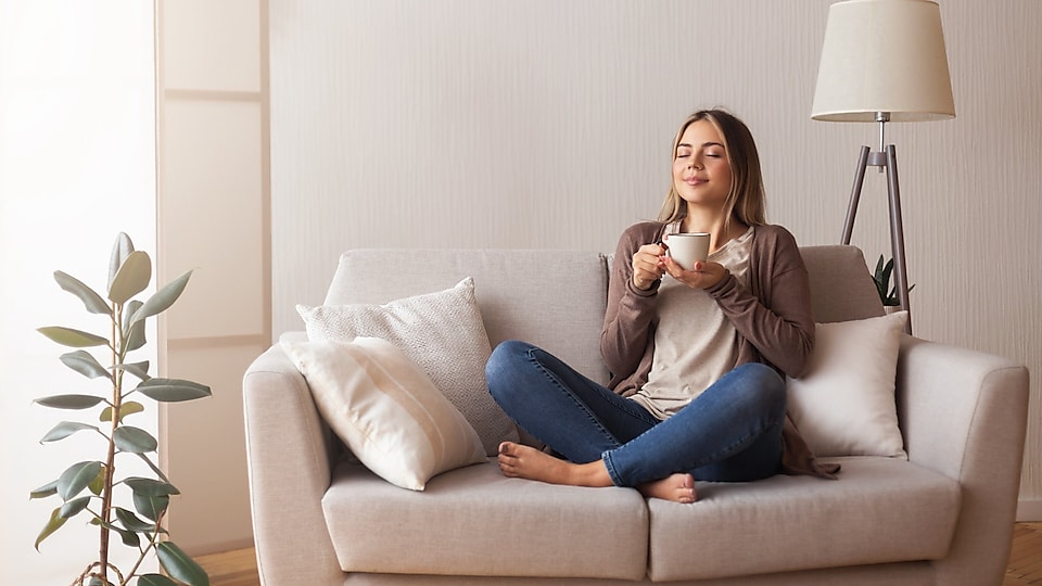 Frau im Schneidersitz auf dem Sofa mit einer Tasse in der Hand