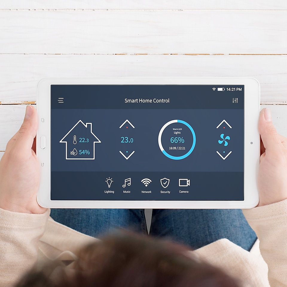 Ein Mensch hält ein weißes Tablet mit diversen Zahlen, Grafiken und Icons. Die Schritft „Smart Home Control“ ist zu lesen.